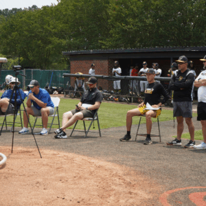 A group of college baseball coaches evaluating live at-bats at a Committed Baseball Showcase event