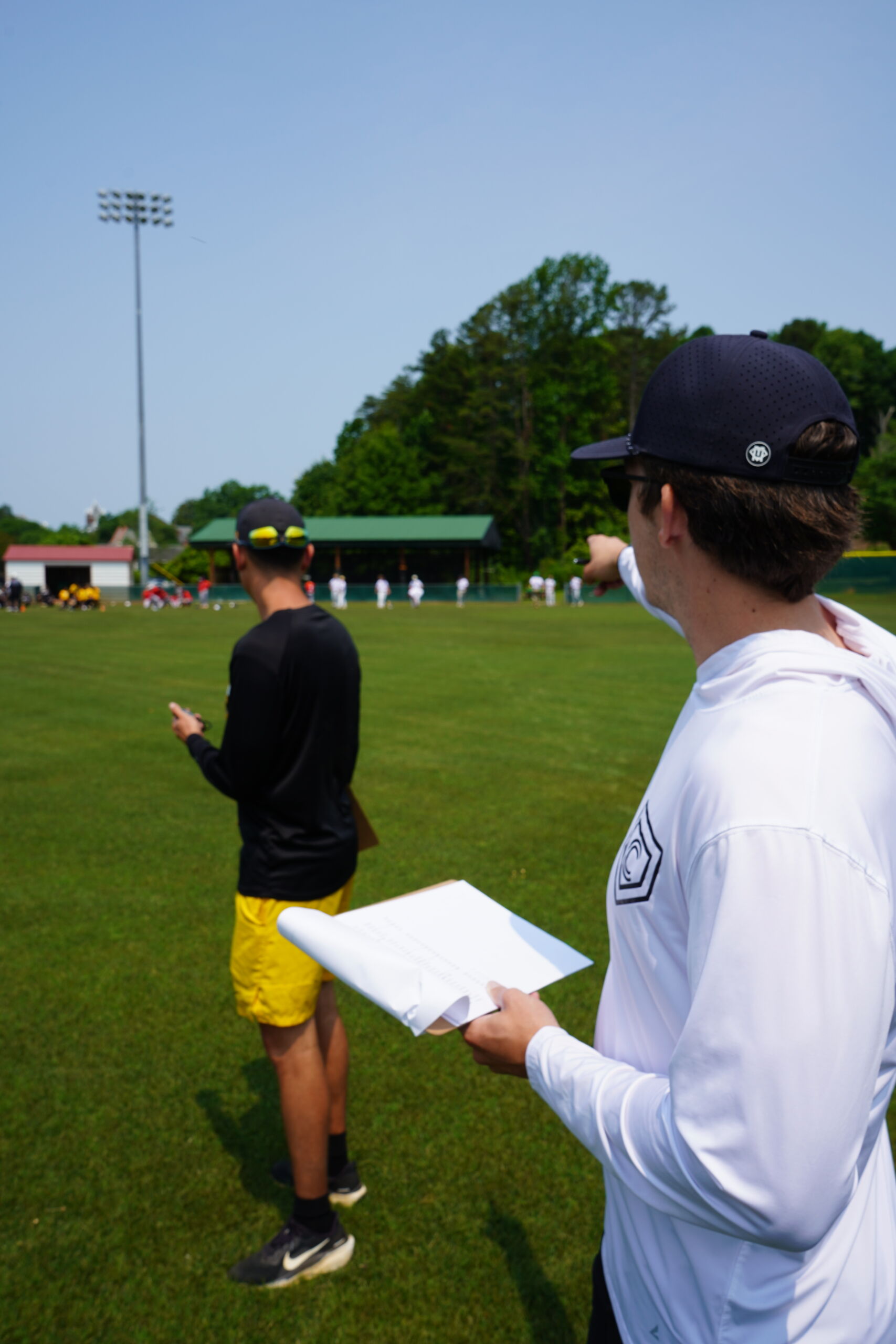Committed Baseball Showcase staff members organize athletes and record data during 60-yard dash testing on outfield grass.