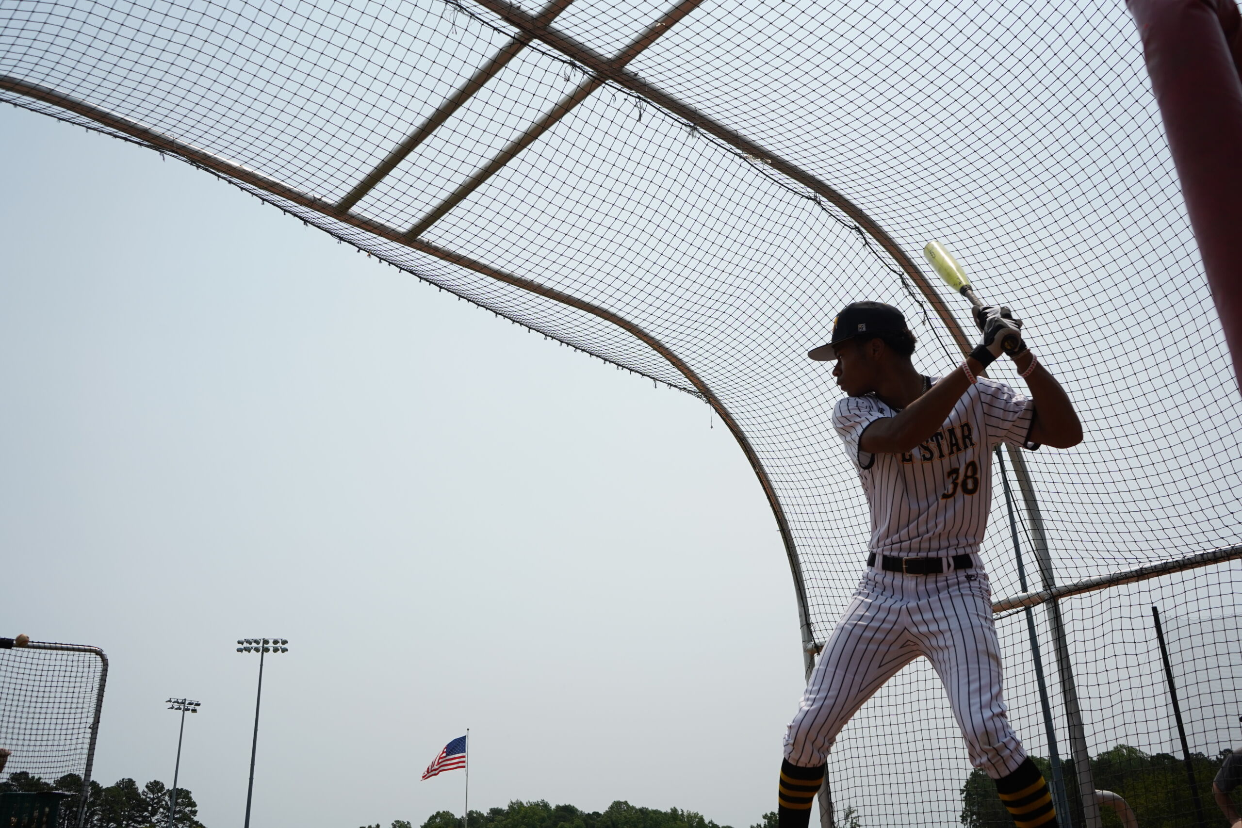 Baseball player in striped uniform prepares to hit during batting cage session at Committed Baseball Showcase.
