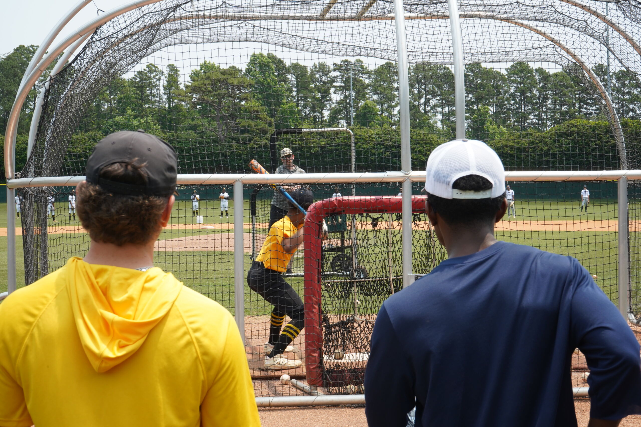Baseball prospect takes swing in batting cage as college coaches observe closely during live BP at Committed Baseball Showcase.