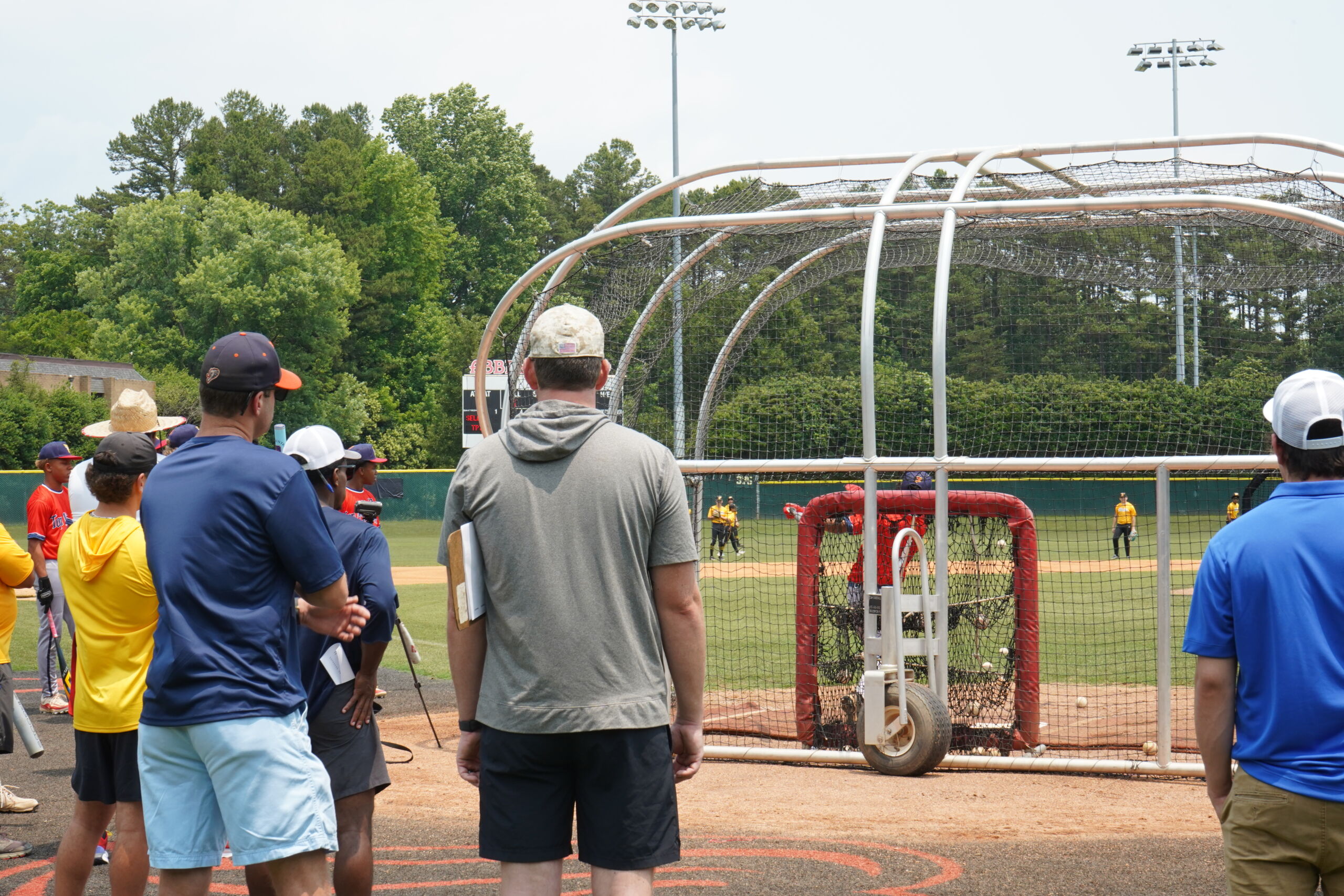 College coaches and staff observe batting practice from behind the cage during Committed Baseball Showcase hitting evaluations.