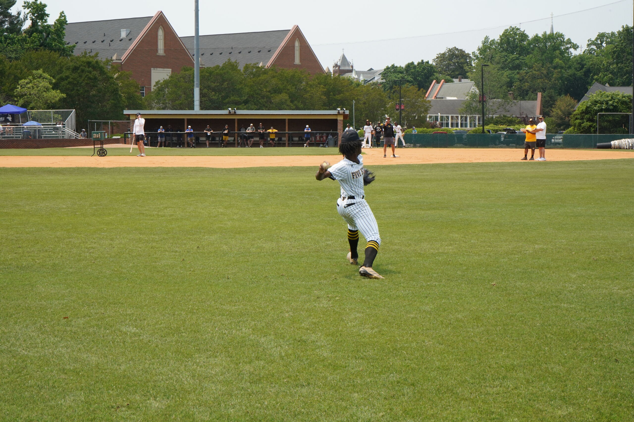 Outfielder makes a throw to infield during defensive drills at Committed Baseball Showcase as coaches and players watch from dugout.