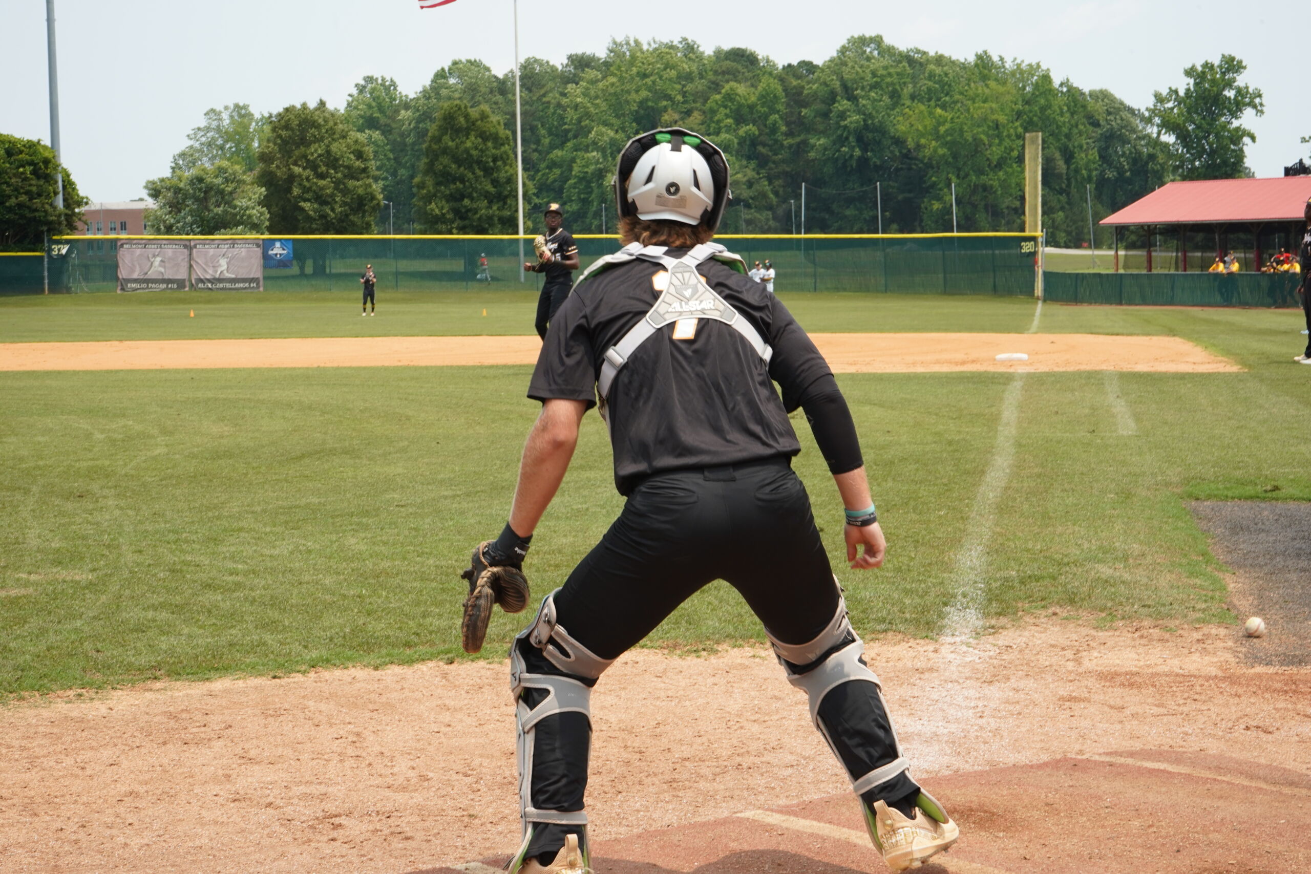 High school catcher receiving throw during Committed Baseball Showcase defensive workout with coaches evaluating from behind the plate.